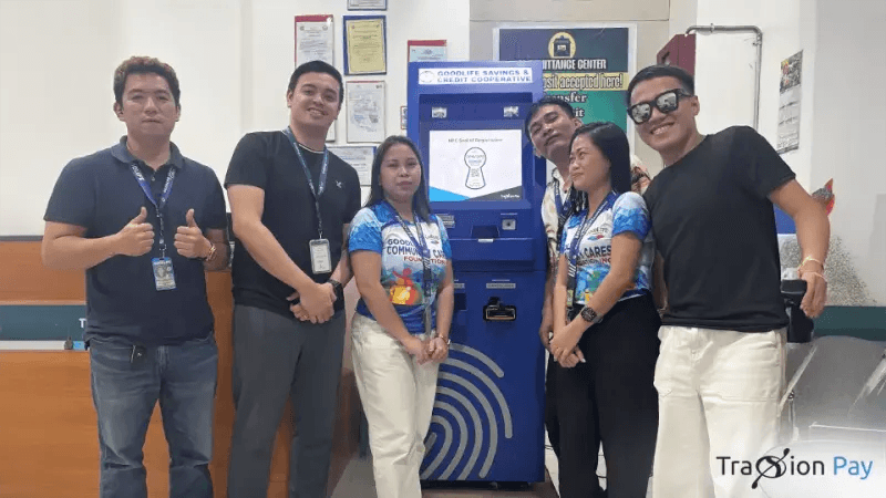 Goodlife Savings Credit Cooperative staff and TraxionPay representatives beside the cooperative's Cash Teller Machine, two giving a thumbs-up.